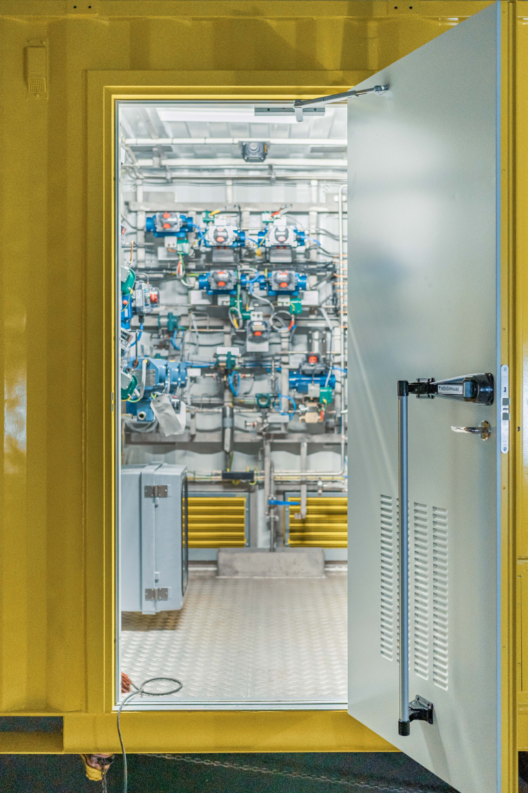 Öppen dörr till en gul container med teknisk utrustning och ventiler installerade på insidan