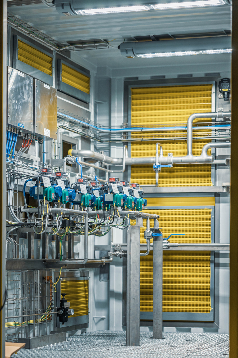 Industriell installation i en container med automatiska ventiler, rörledningar och gula ventilationsgaller